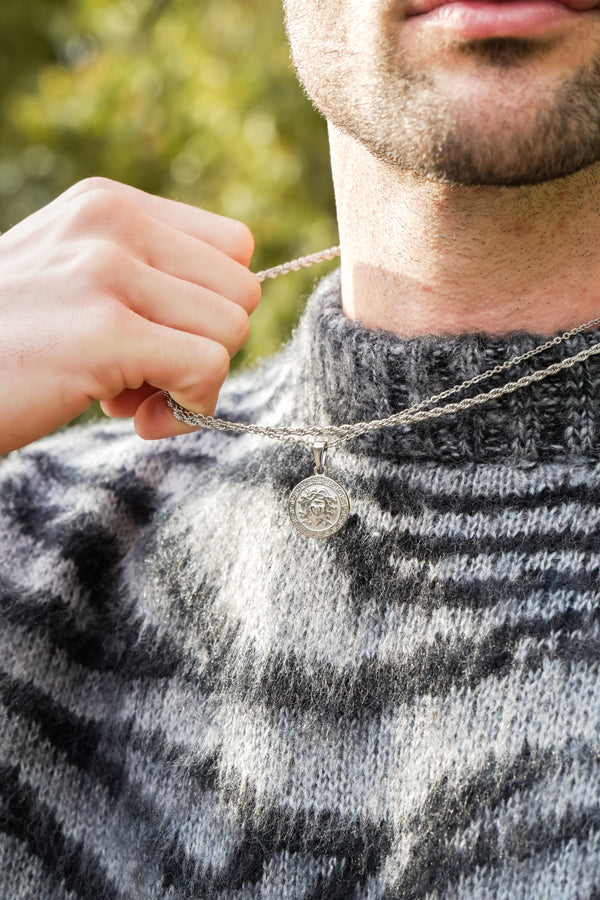 man holding chain wearing a knit jumper with leaves in background