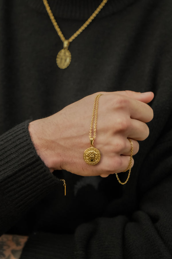 man holding a pendnat with gold chain in his fist whilst wearing a pendant and chain in the background